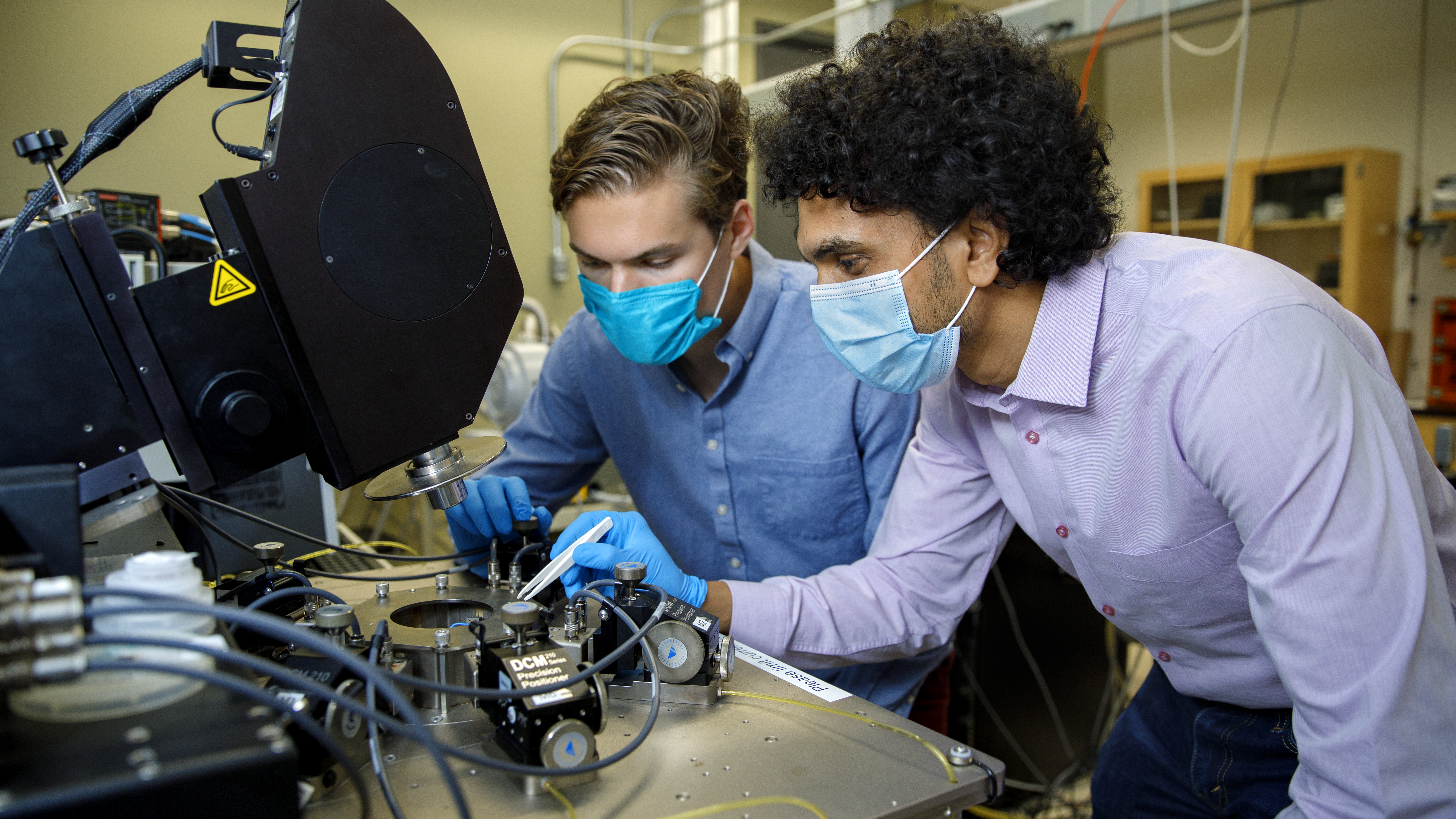 two people wearing masks look through a microscope